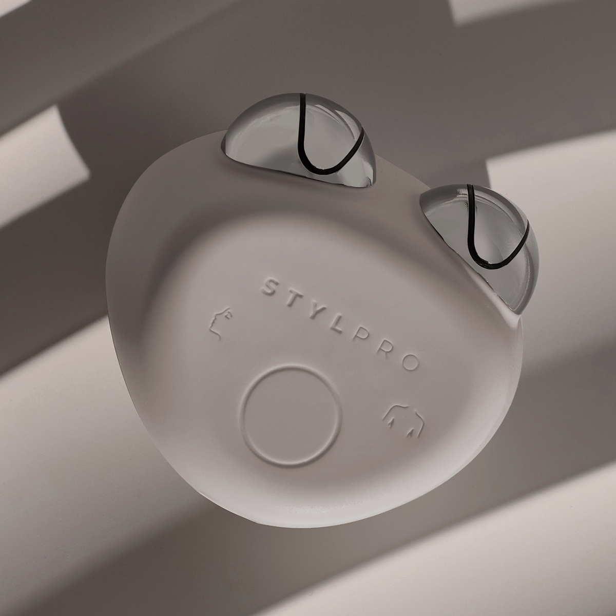 Das STYLPRO Dual Microcurrent Face & Body Toning Device mit zwei silbernen Edelstahlkugeln auf einer grauen Oberfläche mit Schattenmustern.
