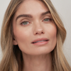 Ein Model mit langen blonden Haaren trägt SWEED Air Blush Cream und ein natürliches Make-up und blickt vor einem schlichten Hintergrund in die Kamera.