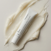 Transparente Lab Lip Renewal-Tube auf einem Cremeabstrich, von oben gesehen vor einem neutralen Hintergrund.