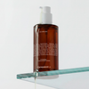 Eine braune Pumpflasche mit Melanoil DHA von Transparent Lab mit Öl, das aus einem Glasregal darunter tropft.