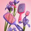 Vier Unbrush- und Super Mini Set Neon Pink-Haarbürsten in Rosa und Lila, präsentiert inmitten von violetten Irisblüten.