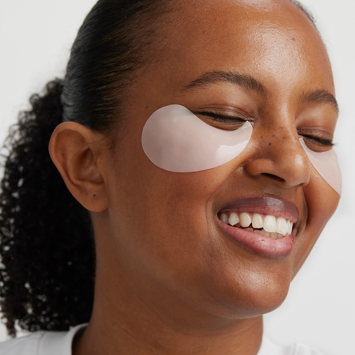 Eine lächelnde Frau trägt XLASH Awakening Eye Gels und präsentiert damit ihre gesunde, strahlende Haut.