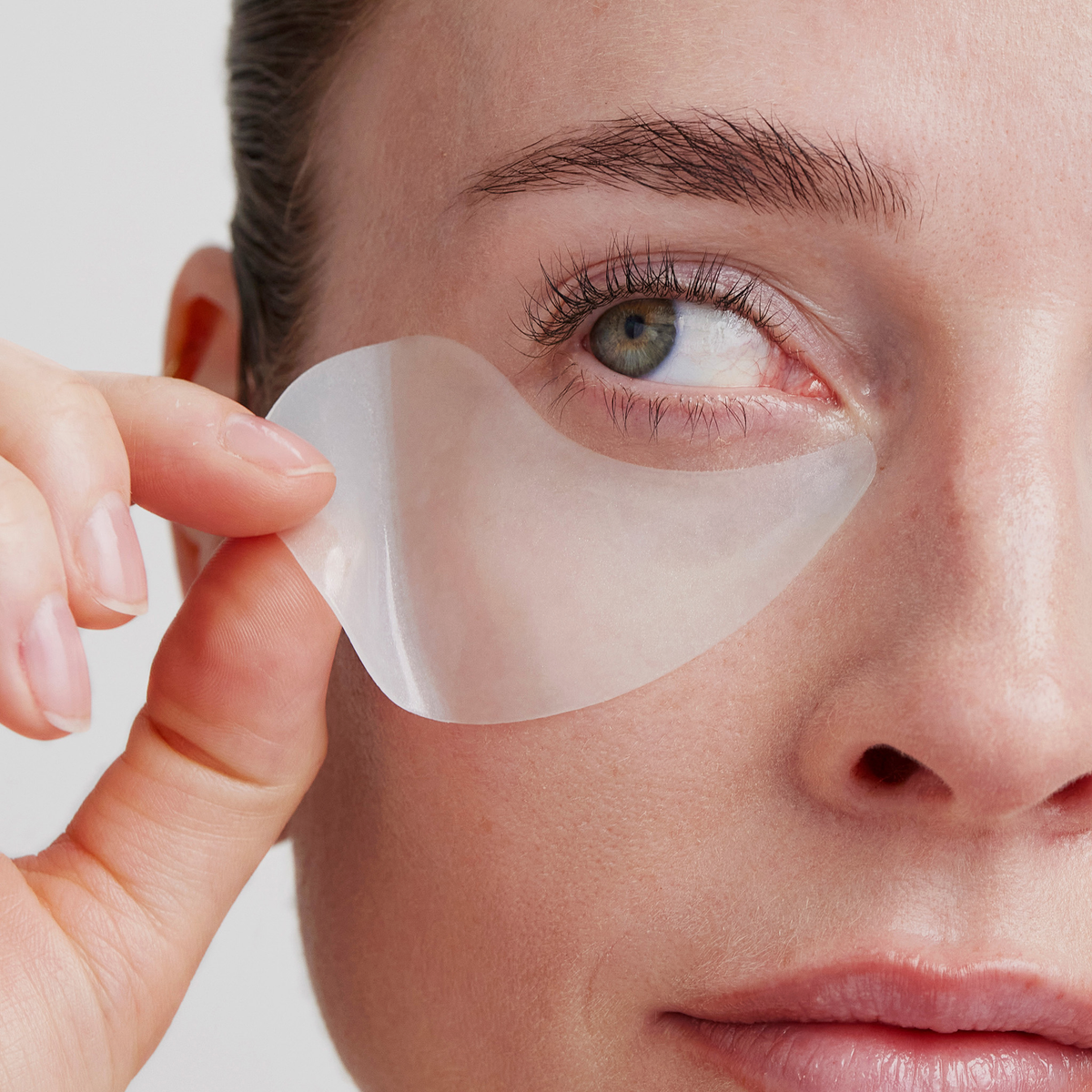 Nahaufnahme einer Person, die mit der linken Hand XLASH Rejuvenating Eye Gels unter ihrem rechten Auge aufträgt.