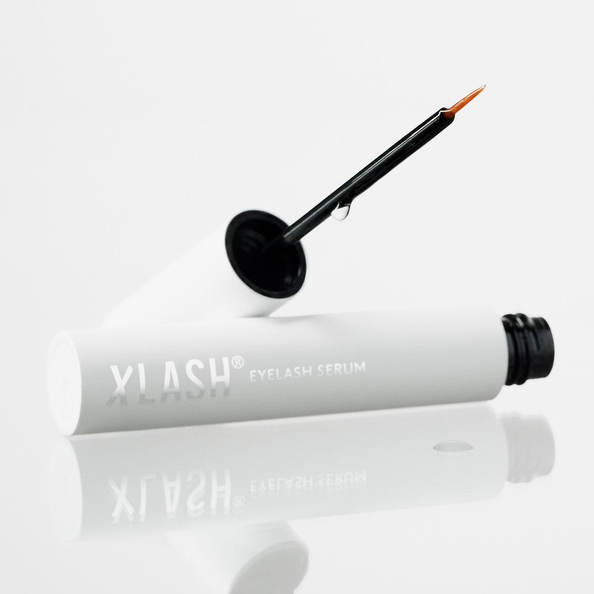 Xlash Eyelash Serum mit Applikatorstift und einem Tropfen auf der Bürste, abgebildet auf weißem Hintergrund.