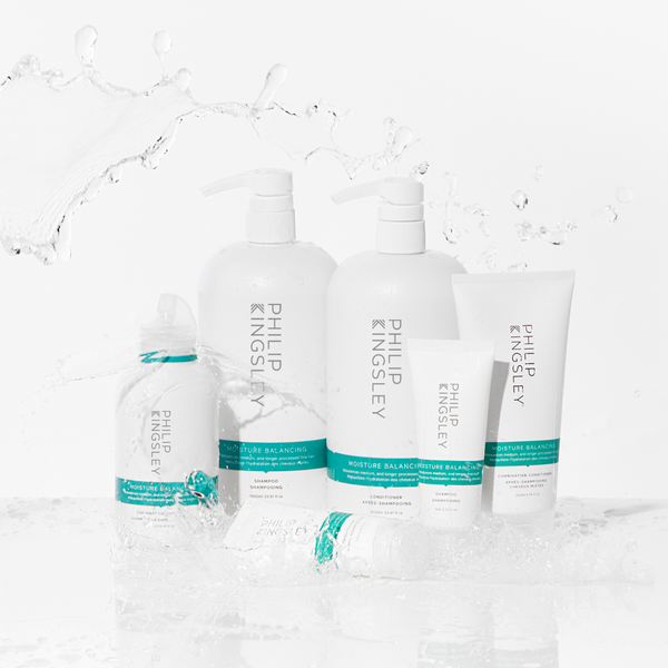 Sechs Haarpflegeprodukte von Philip Kingsley mit türkisfarbenen Etiketten sind auf einer nassen Oberfläche angeordnet, im Hintergrund spritzt Wasser.