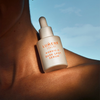 Eine Flasche Lumene Nordic-C Dark Spot Serum ruht auf dem Schlüsselbein einer Person vor einem blauen Himmel.