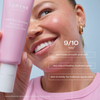 Lächelnde Frau, die Lumene Nordic Bloom Bounce Moisturizer in der Nähe ihres Gesichts hält, Text zu den Vorteilen der Feuchtigkeitspflege überlagert das Bild.