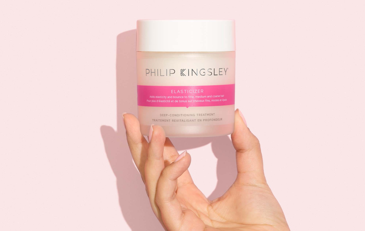 Vor einem rosa Hintergrund hält eine Hand ein Tiegel mit der Intensivpflege „Elasticizer“ von Philip Kingsley in der Hand.