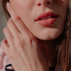 Eine Frau streicht sich im Sonnenlicht über das Gesicht und trägt dabei „BLONDESISTER 2 IN 1 IT’S UP TO YOU LIP OR CHEEK“ für einen natürlichen Glanz.