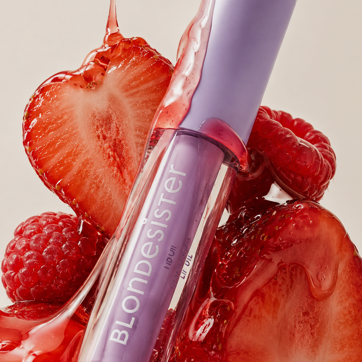 Eine „BLONDESISTER 3 IN 1 CUTE LIPPY LIP OIL“-Tube mit Himbeer-, Erdbeer- und roten Farbspritzern im Hintergrund.