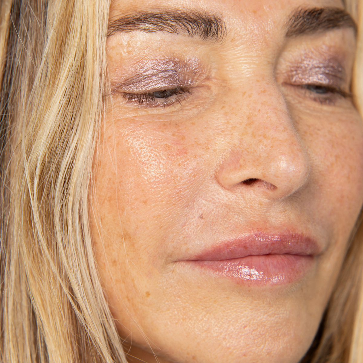 Eine Nahaufnahme zeigt eine Frau, die den Lidschatten „BLONDESISTER GLOWEYE“ trägt, mit natürlichem Teint und hellrosa Lipgloss.
