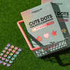 Zwei Schachteln Cute Dots gegen Hautunreinheiten und Pickel sowie ein Bogen mit stern- und blumenförmigen Aufklebern in einem kleinen Einkaufskorb aus Metall auf dem Rasen.