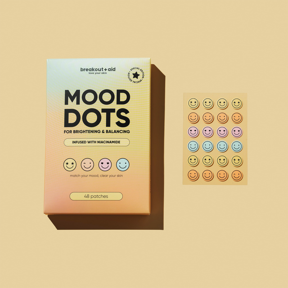 Eine Schachtel mit Mood Dots-Niacinamid-Pflastern neben einem Bogen mit bunten Aufklebern mit Smileys.