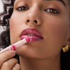 Frau trägt mit einem Applikator ein glänzendes pinkes Lip Oil auf ihre Lippen auf, Nahaufnahme mit Fokus auf Lippen und Produkt.