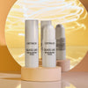 Zwei Catrice Glass Like Highlighter Sticks auf runder Podestfläche vor Spiegel und goldenem Hintergrund, einer mit geöffnetem Stick, einer mit Deckel.