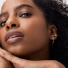 Nahaufnahme eines Gesichts mit natürlichem Make-up, definierten Wimpern und goldenen Ohrringen, die Hand stützt sanft das Kinn.