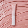 Eine Tube Catrice Cosmetics Under Eye Brightener Liquid auf einem strukturierten, hellrosa Hintergrund.