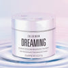 Ein silbernes Gefäß mit Color Wow Dreaming Treatment ruht auf plätscherndem Wasser vor einem weichen pastellfarbenen Hintergrund.