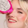 Lächelnde Frau hält Juicy Lip Balm von Dominique Cosmetics in der Nähe ihres Auges vor einem hellen Hintergrund.