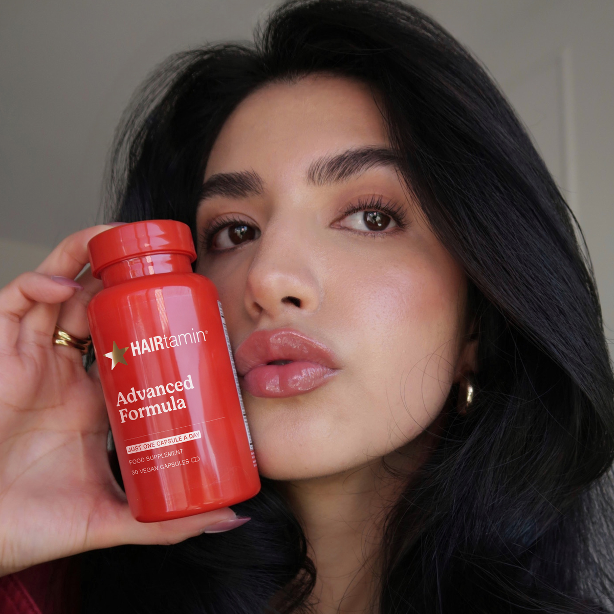Eine Frau mit langen, dunklen Haaren hält eine Flasche „HAIRtamin Advanced Formula“ für einen Monat nahe an ihr Gesicht, die Lippen sind leicht geöffnet.
