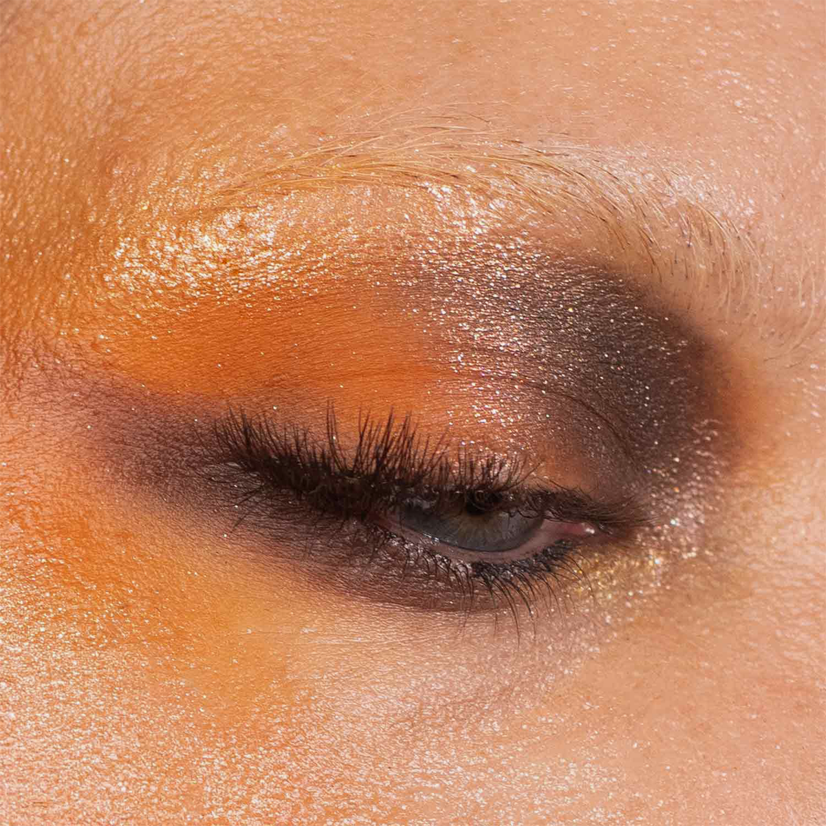 Eine Nahaufnahme eines geschlossenen Auges mit orangefarbenen und braunen Schimmerpartikeln aus der „Over The Garden Wall“-Palette von Lethal Cosmetics; die Wimpern sind zu sehen.