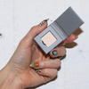 Eine Hand mit farbenfroher Nagelmalerei hält LH Cosmetics' The Single compact mit hellbeigem Puder vor einem weißen Hintergrund.