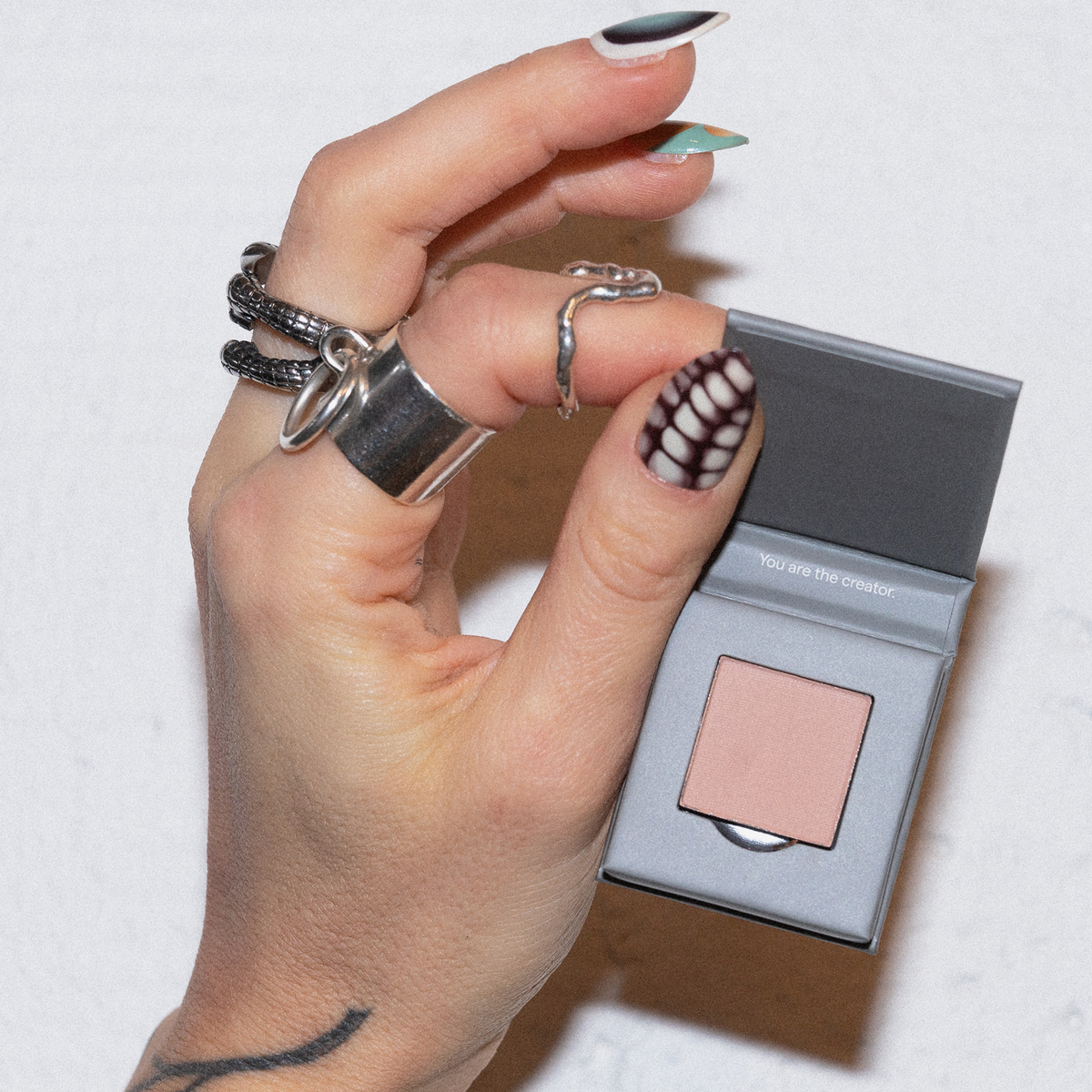 Eine Hand mit Ringen und Nailart hält eine geöffnete LH Cosmetics The Single Kompaktdose mit Pfirsichpuder.