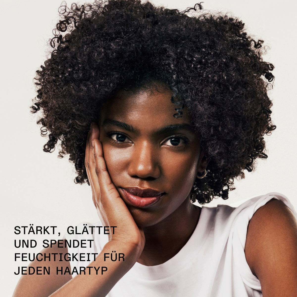 Eine Frau mit starken definierten Locken blickt in die Kamera; daneben Text: "stärkt, glättet und spendet Feuchtigkeit für jeden Hauttyp".