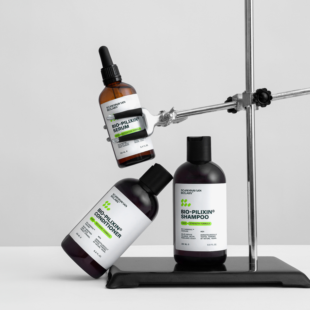 Drei Flaschen Scandinavian Biolabs Bio Plixin Shampoo, Conditioner und Serum+ Men sind auf einem Metallständer vor einem weißen Hintergrund ausgestellt.