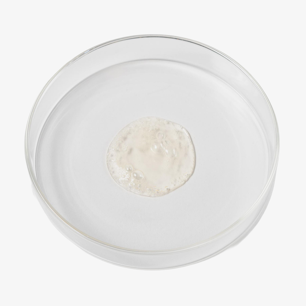 Kleine Menge einer milchigen Flüssigkeit mit feiner Schaumbildung in einer Petrischale.