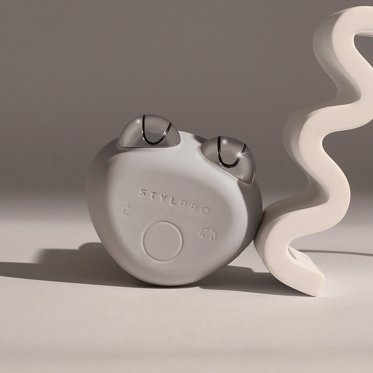 Das STYLPRO Dual Microcurrent Face & Body Toning Device ist neben einer weißen, gewellten Skulptur auf neutralem Hintergrund abgebildet.