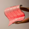 Eine Person hält das STYLPRO Red Light Full Body Panel, das rote LED-Lichter ausstrahlt, vor einen neutralen Hintergrund.