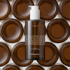 Eine Flasche Transparent Lab Melanoil DHA Serum ist mit braunem Muster der Flaschenunterseiten im Hintergrund abgebildet.
