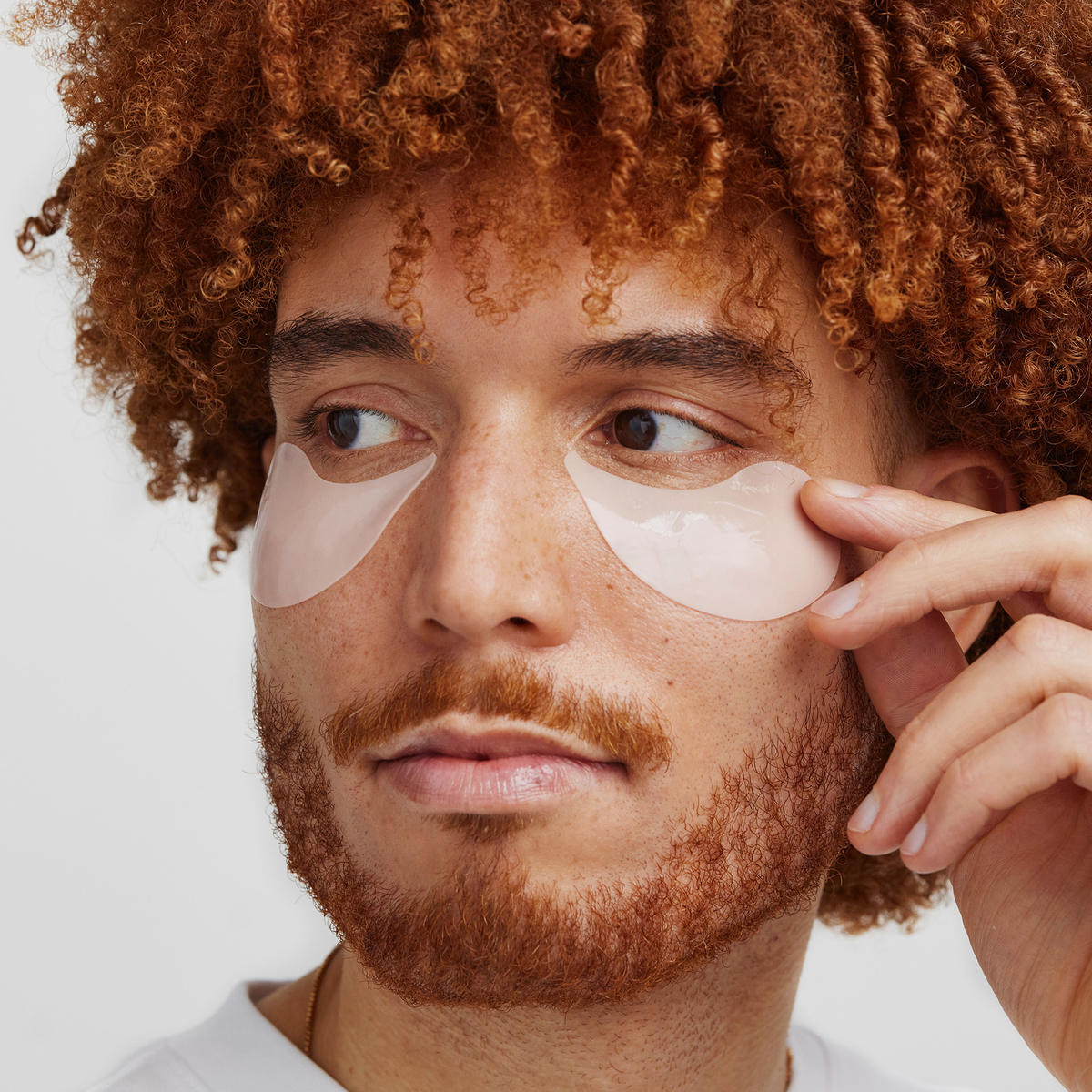 Eine Person mit lockigem Haar trägt XLASH Awakening Eye Gels auf und blickt dabei mit neutralem Gesichtsausdruck zur Seite.