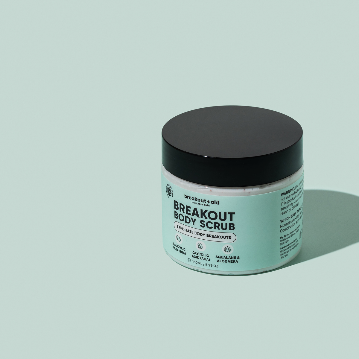 Ein rundes Töpfchen breakout+aid Breakout Body Scrub mit schwarzem Deckel und einem Etikett, auf dem Salicylsäure, Glykolsäure und Squalan aufgeführt sind.