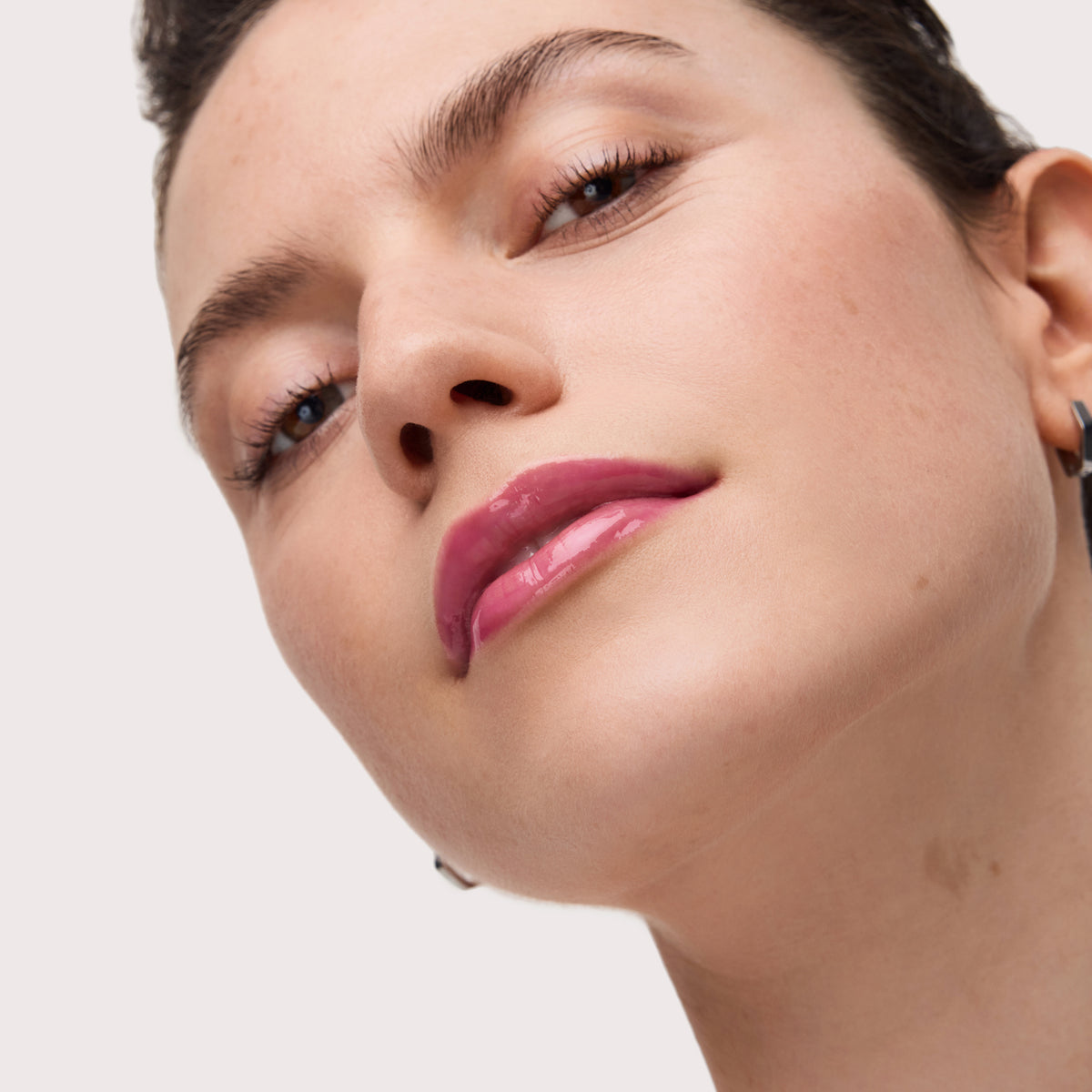 Frau mit glänzendem pinkem Lip Oil auf den Lippen, Nahaufnahme von unten aufgenommen, strahlender, frischer Look.