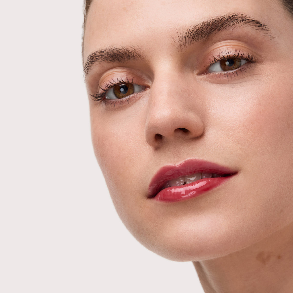 Nahaufnahme eines Gesichts mit glänzendem, kirschrotem Lippenöl und dezentem Augen-Make-up, aufgetragen mit dem Catrice Colour Cushion Lip Oil.