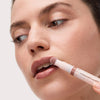Eine Frau trägt mit einem Applikator das Catrice Colour Cushion Juicy Lip Oil in einem natürlichen Braunton auf die Lippen auf.
