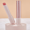 Eine geöffnete Tube des Catrice Cosmetics Diamond Glaze Gloss Stick in Pink wird auf einer strukturierten, runden Oberfläche präsentiert.