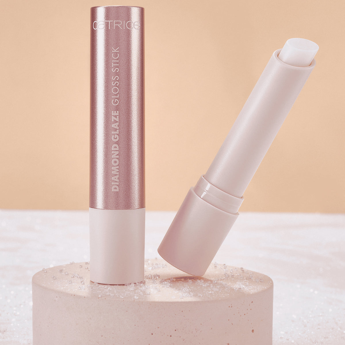 Catrice Diamond Glaze Gloss Stick in einem sWeißton, geöffnet mit sichtbarer Produktspitze, neben geschlossenem Stick auf hellem Podest.