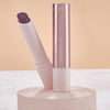 Catrice Diamond Glaze Gloss Stick in einem schimmernden dunklen Beerenton, geöffnet mit sichtbarer Produktspitze, neben geschlossenem Stick auf hellem Podest.