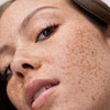 Nahaufnahme einer Frau mit Sommersprossen, neutralem Make-up und braunem Haar, die leicht nach oben schaut .