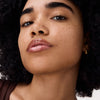 Nahaufnahme eines Gesichts mit Locken und Sommersprossen, die Lippen glänzen dank aufgetragener pflegender Lippenmaske in einem zarten Rosaton.