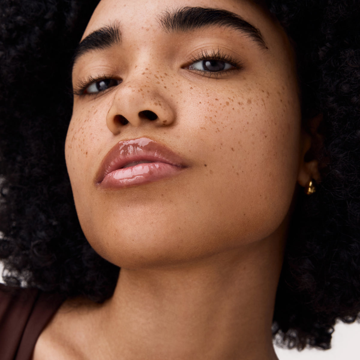 Nahaufnahme eines Gesichts mit Locken und Sommersprossen, die Lippen glänzen dank aufgetragener pflegender Lippenmaske in einem zarten Rosaton.