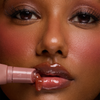 Eine Frau trägt den Dominique Cosmetics Juicy Lip Balm auf und zeigt dabei glänzende rosa Lippen und glatte Haut.