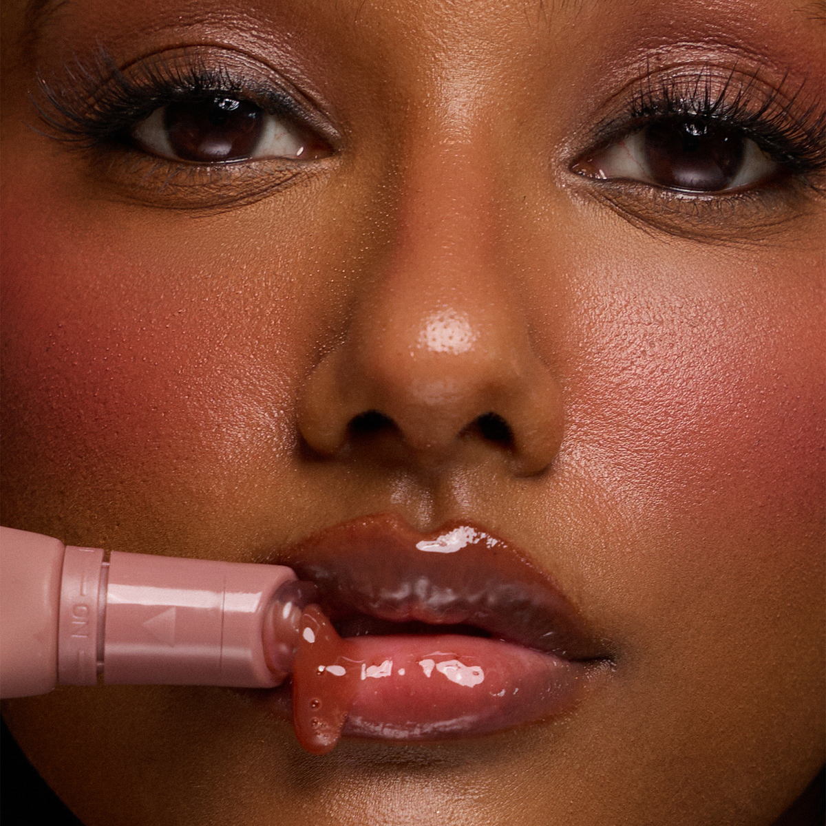 Eine Frau trägt den Dominique Cosmetics Juicy Lip Balm auf und zeigt dabei glänzende rosa Lippen und glatte Haut.