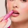 Eine Frau trägt Dominique Cosmetics Juicy Lip Balm auf ihre Lippen auf und hält die Tube in der Hand.