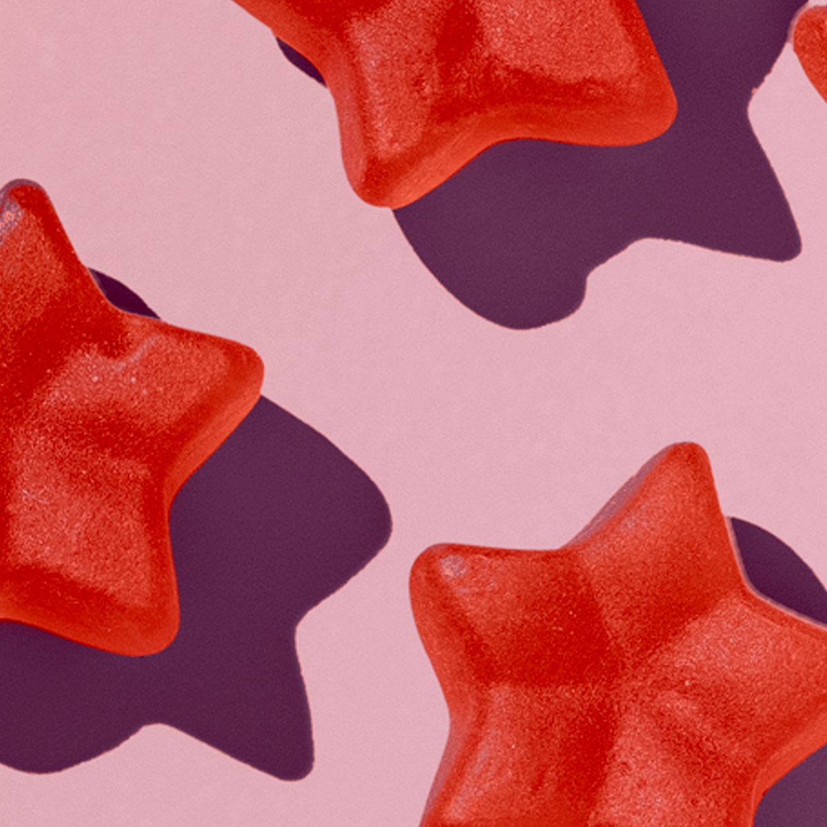 Rote, sternförmige Hairtamin Gummies auf rosafarbenem Hintergrund, Detailaufnahme mit weicher Textur und Schatten.
