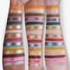 Auf drei Unterarmen sind Farbmuster der Lidschatten aus der „Over The Garden Wall – Tome of the Unknown“-Palette von Lethal Cosmetics zu sehen.