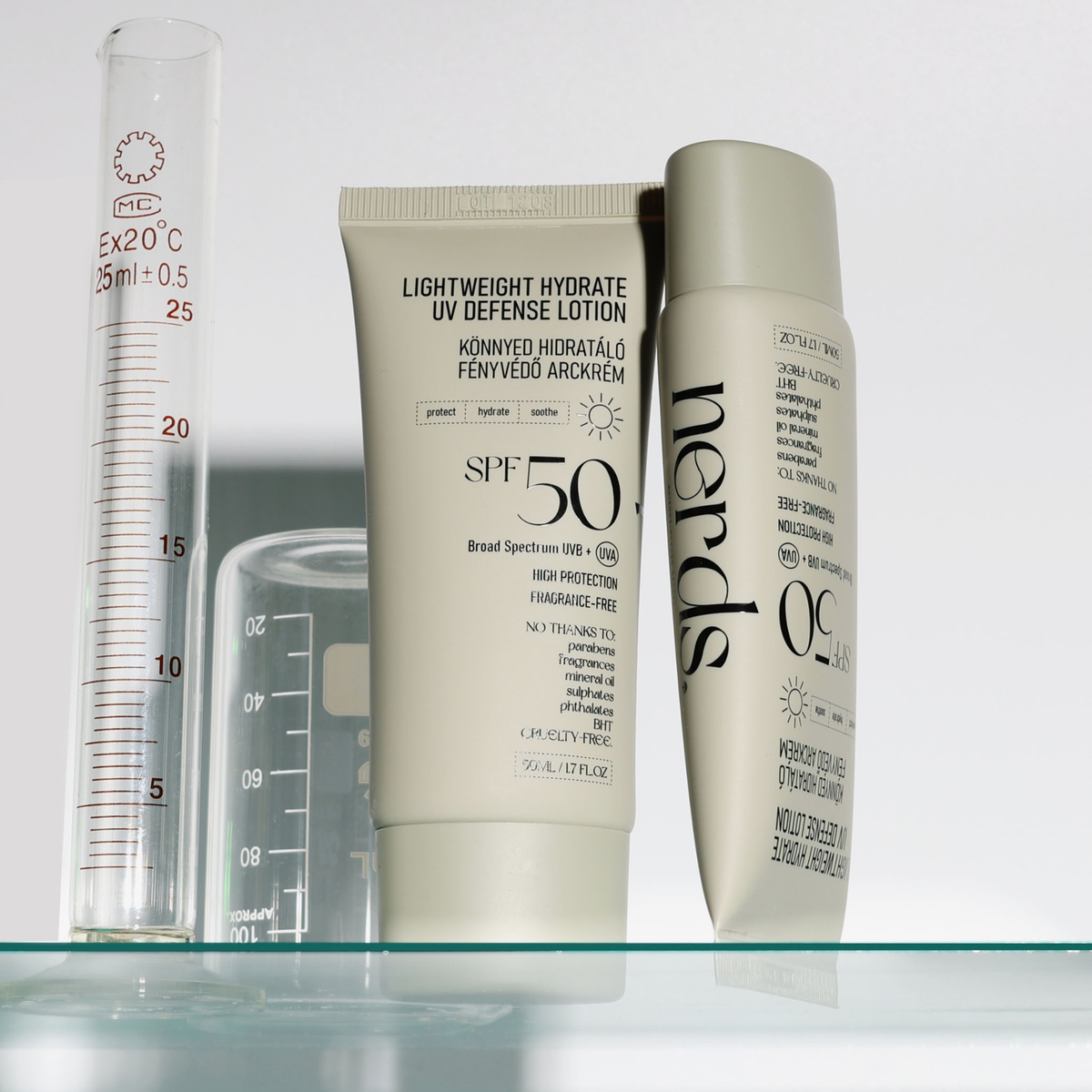 Zwei Flaschen der NERDS. Lightweight Hydrate UV Defense Lotion SPF50 und ein Glasmesszylinder auf einer Glasfläche.